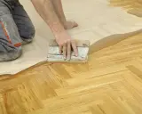 Un artisan applique un produit sur un parquet en chevrons. Une étape essentielle pour la réparation parquet.