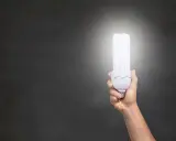 Dłoń trzymająca energooszczędną żarówkę o mocy 806 lumenów, rozświetlającą ciemne tło.