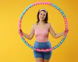 Uśmiechnięta kobieta z hula hop. Dowiedz się, jak dobrać hula hop do wzrostu, by ćwiczenia były efektywne i przyjemne.