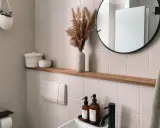Étagère en bois dans une salle de bain carrelée, avec des décorations et un miroir rond.
