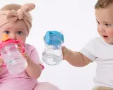 Dzieci z zaciekawieniem patrzą na swoje pierwsze butelki do picia wody. Jedno dziecko trzyma różową, drugie niebieską.