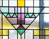 Un motif géométrique coloré orne cette fenêtre vitraux, mêlant le jaune vif, le violet doux et le vert émeraude.