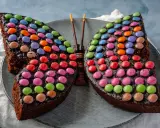 Ein schokoladiger Smarties Kuchen in Form eines Schmetterlings, der mit bunten Smarties dekoriert ist.