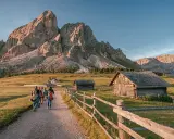 Piękna fotografia krajobrazowa Dolomitów. Grupa turystów wędruje ścieżką obok drewnianych chat, pod majestatycznymi szczytami górskimi.