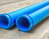 Dwie niebieskie rury PVC leżą na betonie. To idealna jaka rura do przyłącza wody, gotowa do montażu.