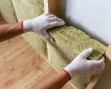 Pose d'isolant en laine de roche dans une structure en bois. Une bonne isolation intérieure et extérieure prévient le point de rosée.