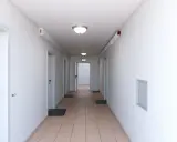 Ein langer, heller Flur mit mehreren Türen und einem grünen Notausgangsschild. Dieser notwendiger Flur ist gut beleuchtet und wirkt einladend.