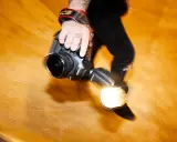 Dłoń fotografa trzyma aparat z lampą błyskową. Długi czas naświetlania tworzy efekt ruchu.