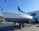 Voilier blanc sur bers, coque bleue usée, sous un ciel clair. Le mât est dressé, la grand-voile bleue enroulée. Premier 29 avis.