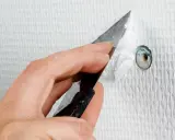 Hand spacklar ett hål i en vit, strukturerad vägg med en spackel.