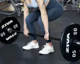 Donna in palestra si prepara per gli stacchi da terra con un bilanciere.