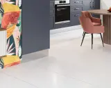 Białe płytki lappato w kuchni z kolorową ścianą i różowym krzesłem.