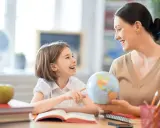 Niña y maestra sonríen mientras exploran un globo terráqueo. Un ejemplo de como ser un buen profesor, inspirando curiosidad y aprendizaje.