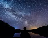 Zachwycająca fotografia astronomiczna Drogi Mlecznej nad jeziorem. Sylwetka człowieka kontempluje kosmos.