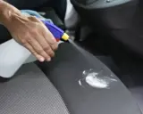 Mano rocía un asiento de coche con un limpiador para eliminar manchas de flujo.