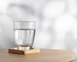 Szklanka czystej wody na drewnianej podstawce. Woda nie ma kalorii, to idealny napój dla zdrowia.