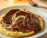 Fette di carne brasata su polenta cremosa, guarnite con cipolle caramellate e rosmarino. Un classico tra i piatti tipici veneti.
