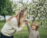 Matka i dziecko w kwitnącym sadzie. Dziecko podaje mamie kwiatki, jakby ilustrowało przysłowia o miesiącach.