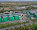 Grüne Biogas-Behälter und große Gasspeicher prägen diese Anlage, die die **Biogas Zukunft** symbolisiert. Im Hintergrund ein Fluss und bewaldete Ufer.