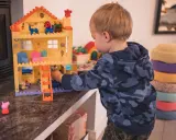 Kleiner Junge spielt mit einem Puppenhaus. Ein Schritt beim **Kinderzimmer ausmisten** ist, Spielzeug zu sortieren.