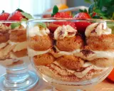Pyszne tiramisu w pucharkach, przełożone kremem, biszkoptami i posypane kakao, ozdobione truskawkami i miętą.