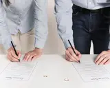 Para dwojga podpisuje dokumenty rozwodowe. Dwa obrączki leżą na stole.