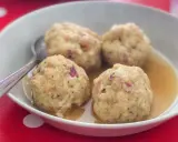 Canederli in brodo, uno dei piatti tipici del Trentino Alto Adige, serviti in una ciotola bianca su un tovagliolo rosso a pois bianchi.