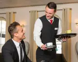 Un serveur souriant présente une tasse de café à un client, illustrant le protocole de service à table.