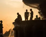 Silhouette fotografia di persone che si rinfrescano in una fontana al tramonto, con l'acqua che scintilla contro il cielo arancione.