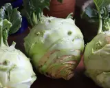 Tre färska kålrabbi, redo för ett gott kålrabbi recept. Gröna blad sticker upp från de ljusgröna rotfrukterna.