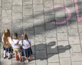 Trójka dzieci w szkolnych strojach patrzy na napis "szkoła społeczna co to" narysowany kredą.