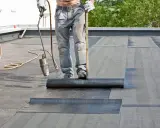 Dachdecker verlegt mit Brenner und Rolle Bitumenbahnen auf einem Flachdach.