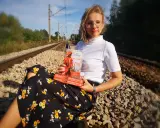 Kobieta z książką "Nauczycielka z Getta" siedzi na torach. Recenzja książki gwiazd naszych win po angielsku.