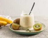 Un verre de smoothie banane kiwi, garni de graines de chia, avec des fruits frais autour.