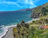 Ein malerischer granada strand mit felsigen Klippen, türkisfarbenem Meer und einer Stadt am Horizont.