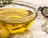 Aceite de oliva vertiéndose en un bol de cristal, rodeado de aceitunas. Varios tipos de aceite comestible para cocinar.