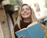 Uśmiechnięta dziewczyna z książką i słuchawkami na ulicy. Może to być studentka, która właśnie skończyła lekcje w szkole w Danii.