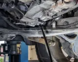 Wymiana oleju w skrzyni manualnej. Mechanik spuszcza stary olej z przekładni.