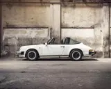 Weißer Porsche 911 3.2 Carrera Targa, ein Klassiker mit stabiler Wertentwicklung, steht in einer alten Lagerhalle.
