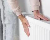 Dłonie sprawdzają temperaturę grzejnika, który słabo grzeje. Zimno w domu, trzeba coś z tym zrobić.