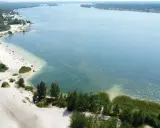 Plaża nad jeziorem, piasek, drzewa i ludzie odpoczywający w słońcu. Idealne miejsce na wakacje, jak z **pogoria** 1.