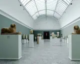 Starożytne rzeźby lwów i popiersi w muzeum w Kopenhadze, podświetlone przez świetlik w dachu.