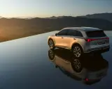 El MG6 EV plateado se refleja en una superficie de agua infinita al atardecer, con montañas al fondo.