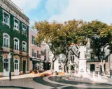 Grüne Kacheln zieren ein Gebäude in der Stadt Lagos. Ein Denkmal steht im Zentrum des Platzes, umgeben von Bäumen und Geschäften.