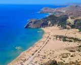 Rodos zachwyca turkusowym morzem i piaszczystą plażą. W oddali widać góry i zabudowania. Idealne miejsce na wakacje.