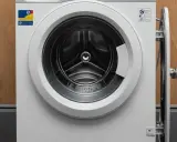 Biała pralka e10 electrolux z otwartymi drzwiczkami, widoczny bęben. Obok drewniana ściana i kable.