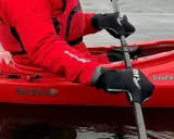 Person i röd jacka och svarta handskar paddlar kajak i kallt vatten.