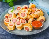 Leckeres Fingerfood für den Sommer: Würstchen im Blätterteig mit Sesam, serviert mit Dip und Ketchup.