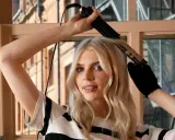 Blondynka tworzy trwałe loki za pomocą lokówki. Jej oczy błyszczą, a włosy falują.