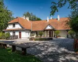 Urokliwy dom z czerwonym dachem w Bronowicach Małych, otoczony zielenią. Widać drewniane ławki i kamienny dziedziniec.